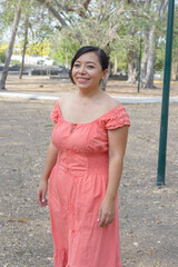 Fototapeta premium A dark-haired young woman smiling while wearing a coral dress with delicate embroidery.