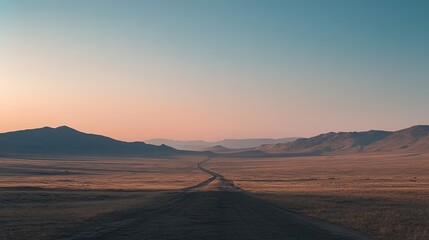 Fototapeta premium A winding dirt road leads through the serene landscape of rolling hills at sunset in a remote location
