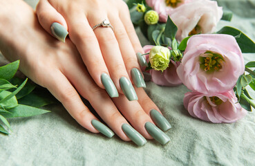 Elegant hands with green nail polish resting on a soft fabric surrounded by delicate flowers in a tranquil setting