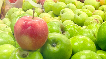 A green apple is sitting on top of a pile of green apples. The apple is red and is the only one of its kind in the pile