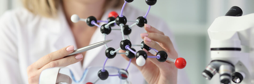 Woman in white lab coat demonstrates model of molecule