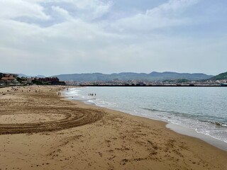 The beach at Getxo, Algorta, Bilao Spain.  View of the mountains in the background.  Unrecognisable people in the background laying on the beach and swimming.