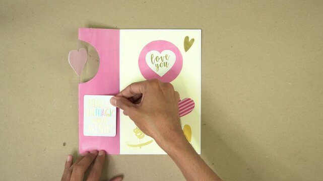 Hand placing sticky note inside handmade Valentine's card with hearts and pastel colors