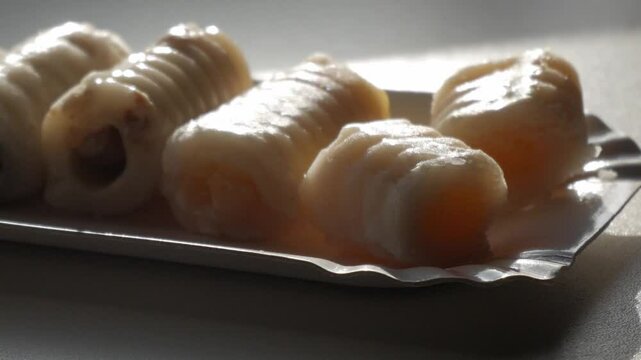 Traditional "huesos de santo" marzipan treats on a tray, backlit by soft daylight