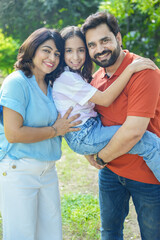 Young happy indian family enjoying in summer park or garden. father carrying, holding her daughter on shoulder. holiday or vacation. Parents with child daughter bonding, love and care.Togetherness.