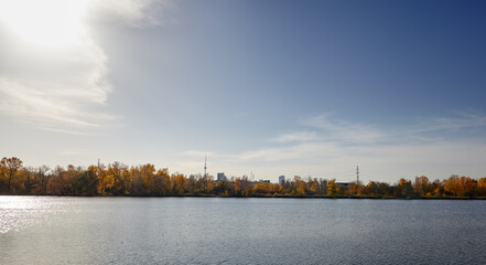 Beautiful european autumnal cityscape landscape. Scenery with dense trees near the river against blue sky background in Kyiv, Europe