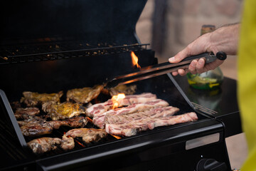 Close up of person grilling meat on barbecue using tongs