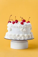 Delicate lambeth style birthday cake with white cream cheese frosting decorated with cocktail cherries on the yellow background