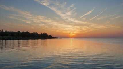 Obraz premium A serene sunset over calm waters at the lakeside, reflecting vibrant colors on a peaceful evening in nature. The sun dips below the horizon, casting warm hues across the sky and water