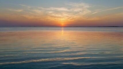 A serene sunset over calm waters at the lakeside, reflecting vibrant colors on a peaceful evening in nature. The sun dips below the horizon, casting warm hues across the sky and water