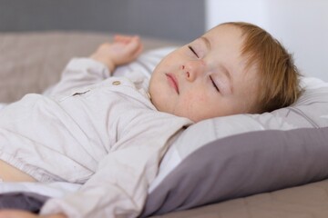 During the day, the child sleeps. The baby is daydreaming, he is lying on a light bed in a beige shirt