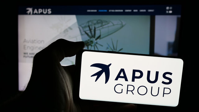 Stuttgart, Germany - 10-22-2024: Person holding smartphone with logo of German company APUS Zero Emission GmbH on screen in front of website. Focus on phone display.