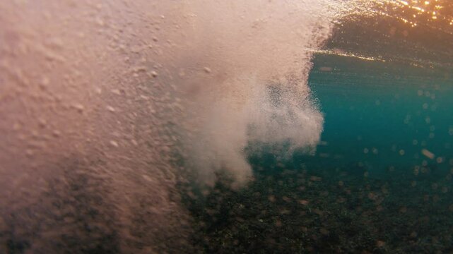 Young man swims in the ocean with waves. Man dives underwater under the breaking ocean wave on sunrise. Person swims in the crushing waves