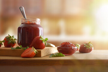 Jars with strawberry jam on wooden table and rustic kitchen