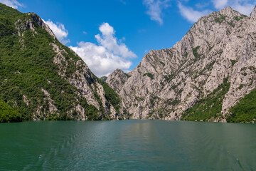 Scenic ferry boat tour on Lake Koman reservoir on Drin river surrounded by forested steep hills,...