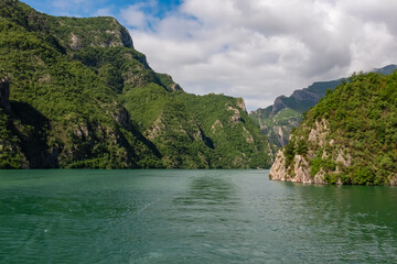 Scenic ferry boat tour on Lake Koman reservoir on Drin river surrounded by forested steep hills,...