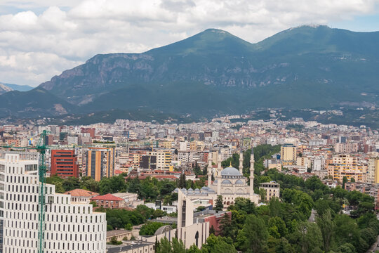 Panoramic view of Tirana city in Albania, nestled between Dajti Mountains and Adriatic Sea. Cityscape is mix of modern high-rises and older buildings, with a mosque and several churches visible