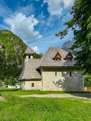 Picturesque stone church of St. George on blooming alpine meadow in calm village Theth, Northern Albania. Surrounded by pine tree forest and steep mountain slopes of Albanian Alps (Accursed Mountains)