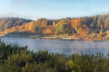 Colorful autumn tree forest behind the river, landscape with fog over the water