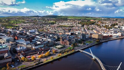 Fototapeta premium City of Derry aka Londonderry in Northern Ireland aerial view - A Dramatic Cityscape by the River Foyle Featuring a Beautiful Pedestrian Bridge
