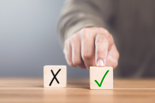 A man choosing between a checkmark and an 'X' symbol on wooden blocks. Image represents the concept of making the right choice, highlighting the importance of distinguishing between right and wrong