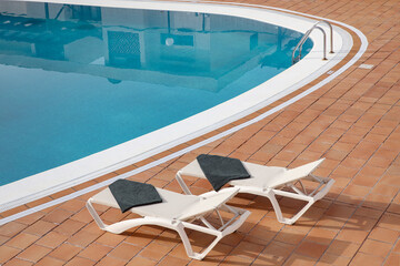 Serene views of a residential swimming pool with a clear blue surface complemented by surrounding terracotta tiles and two white sun lungers neatly positioned nearby, creating a relaxing vacation vibe