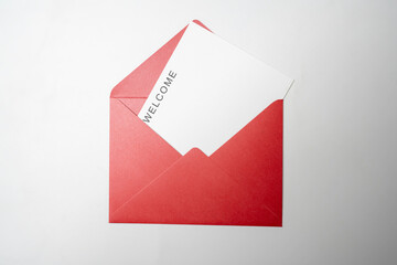 Top view of red envelope and postcard with white card with words Welcome on it. Welcome greeting for invitation, express hospitality, greet, show acceptance