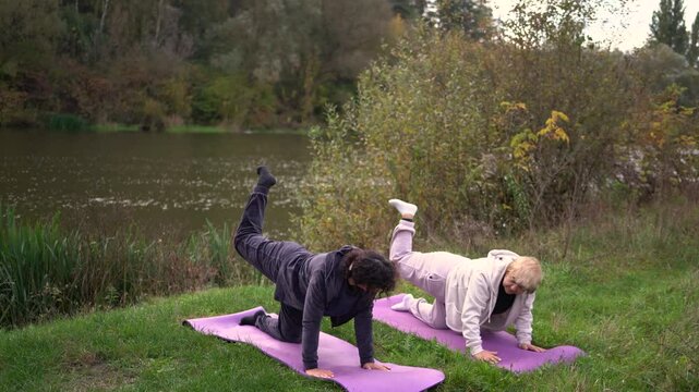 a  middle-aged woman teaches her old mother somatic exercises and yoga to maintain health by the river in autumn