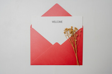 Top view of red envelope and postcard with white card with words Welcome and flowers on it. Welcome...