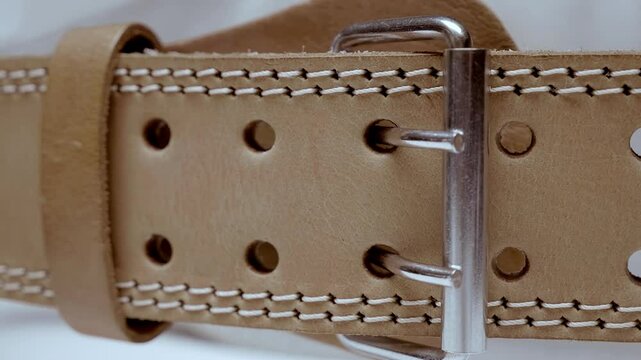 Brown leather belt with double stitching along the edges, even rows of holes and a metal buckle in the middle. Closeup. Macro. Shallow depth of field. Shot in motion