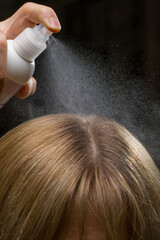 Fototapeta premium Close-up of spraying hair oil on a head of blonde woman.