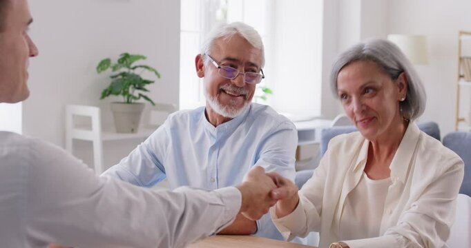 Senior couple of client shaking hands with an agent or consultant during a meeting at home. The gesture signifies agreement and contract, highlighting the successful completion of a deal.