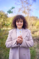 middle-aged woman with dark curly hair in light beige suit and coat enjoying nature in autumn forest