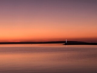 Serene Sunset at Sea with Lighthouse Silhouette Reflecting on Calm Waters