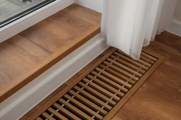 Protective radiator grille built into the floor for heating panoramic windows. Heating grid with ventilation by the floor in hardwood flooring. Side view, copy space. 