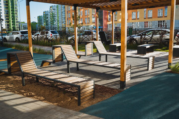 There is a row of comfortable lounge chairs placed strategically under a beautifully designed pergola situated in a serene park, perfect for relaxation and enjoying the outdoors