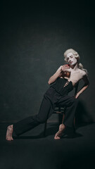 With casual drink in hand, young man with make-up lounges as if he seen audience. Mix of historical aesthetics and modern relaxation makes it unique. Concept of art, music and party, ballet. Ad