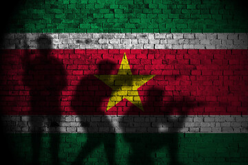 suriname flag on brick wall and soldiers shadow