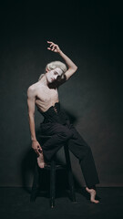 Young man sits with dramatic tilt, embodying both sophistication of history and minimalism of contemporary fashion. Concept of fusion modern and classic, art, music and party, ballet. Ad