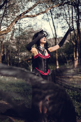 A young woman in the image of a witch and sorceress, standing in a dark forest, wearing a black dress with a train and a socket on her head.