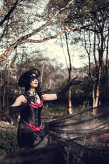 A young woman in the image of a witch and sorceress, standing in a dark forest, wearing a black dress with a train and a socket on her head.