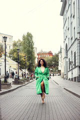 Beautiful stylish young woman with curly dark hair posing in a green trench coat in an urban context. Street fashion and style.