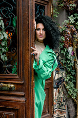 Beautiful stylish young woman with curly dark hair posing in a green trench coat in an urban context. Street fashion and style.