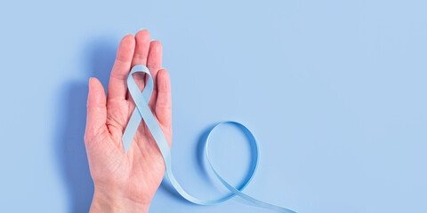 A blue ribbon held gently in both of a womans hands over a matching blue background. The image...