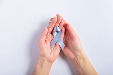 Fototapeta premium A pair of female hands delicately holding a blue cancer ribbon, resting on a white background. A touching representation of support and advocacy for colorectal cancer awareness.