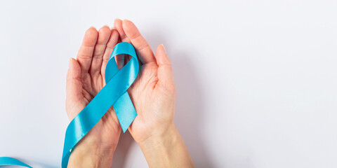 A close-up of a womans hand holding a blue ribbon against a white background, representing...