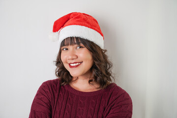 Excited young asian woman wearing santa clause hat and red long sleeved sweater with smiling face expression, isolated over white background. Concept for Christmas Holiday and New Year Party