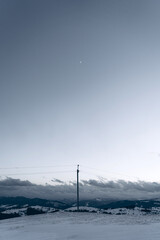 Winter mountain landscape with moon and power line pole under clear sky