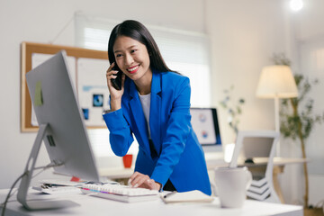 Young businesswoman is multitasking at her desk, talking on her phone while working on her...