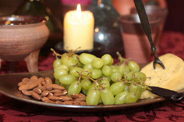 A classic still life composition, elegantly set table reminiscent of traditional castle banquet scenes. The warm glow of a single burning candle illuminates the rustic arrangement of grape